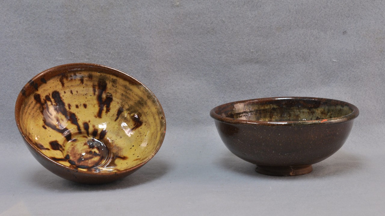 Color photo of two ceramic bowls; the left one is tilted up to show the brown and yellow glaze inside, while the right rests on its base showing its dark brown exterior.