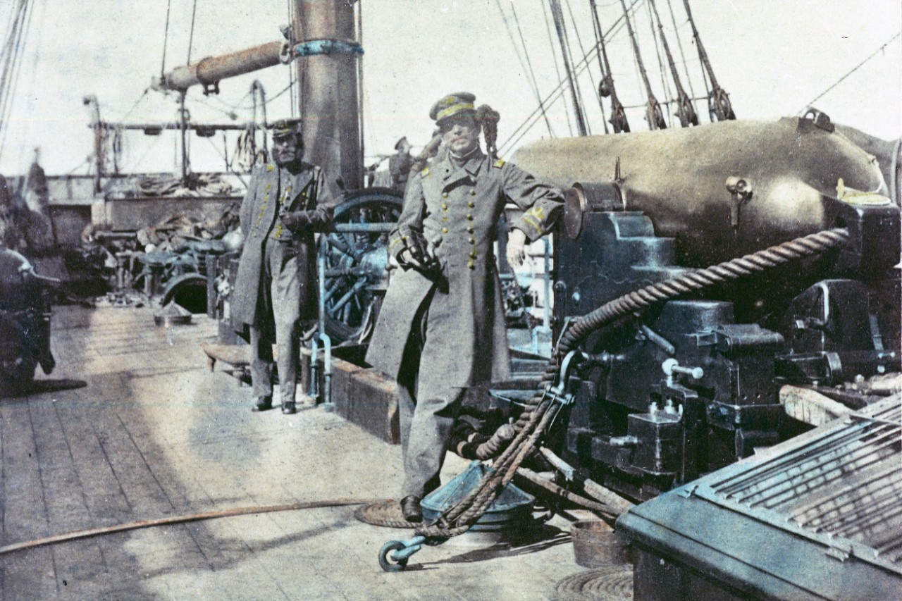 Hand-tinted photograph of two men in Civil War naval uniforms standing on the deck of a ship next to a large cannon.